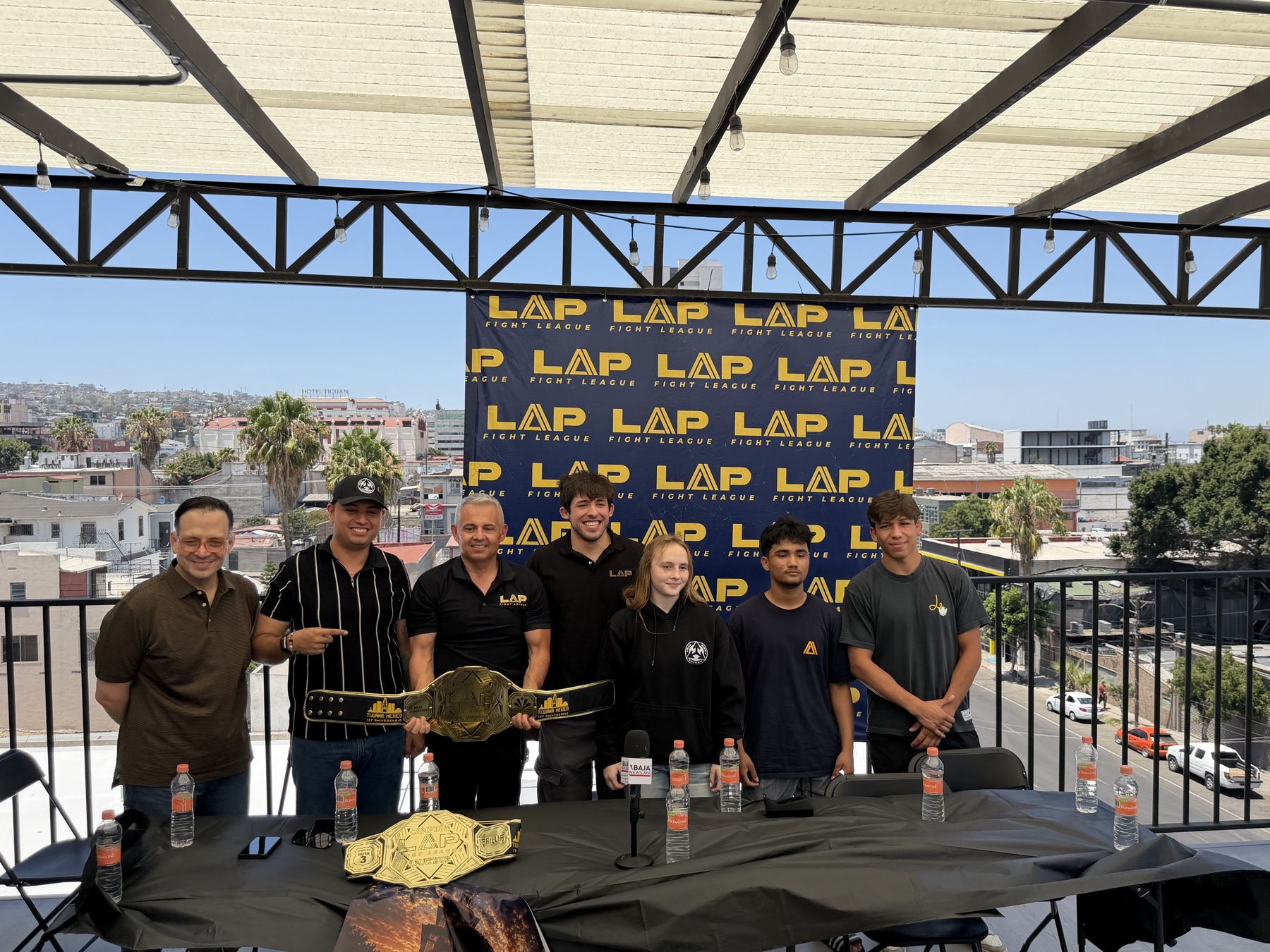 Emma Chandler, al centro de negro, con los organizadores de LAP Fight League y compañeros de cartelera en la conferencia de prensa de LAP 06 en Tijuana, con el cinturón de campeonato sobre la mesa.